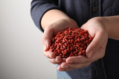 Photo of Woman holding pile of dried goji berries on grey background, closeup. Space for text