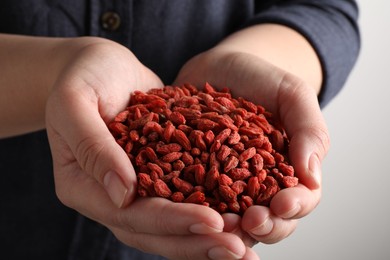 Photo of Woman holding pile of dried goji berries on light background, closeup