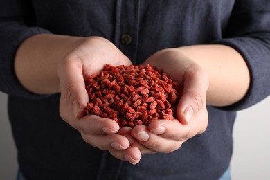 Photo of Woman holding pile of dried goji berries on light background, closeup