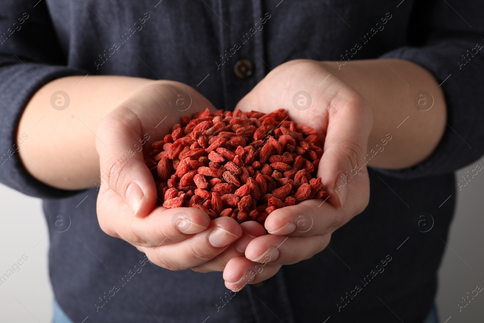 Photo of Woman holding pile of dried goji berries on light background, closeup