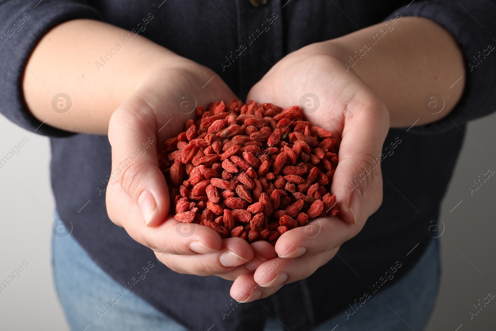 Photo of Woman holding pile of dried goji berries on light background, closeup