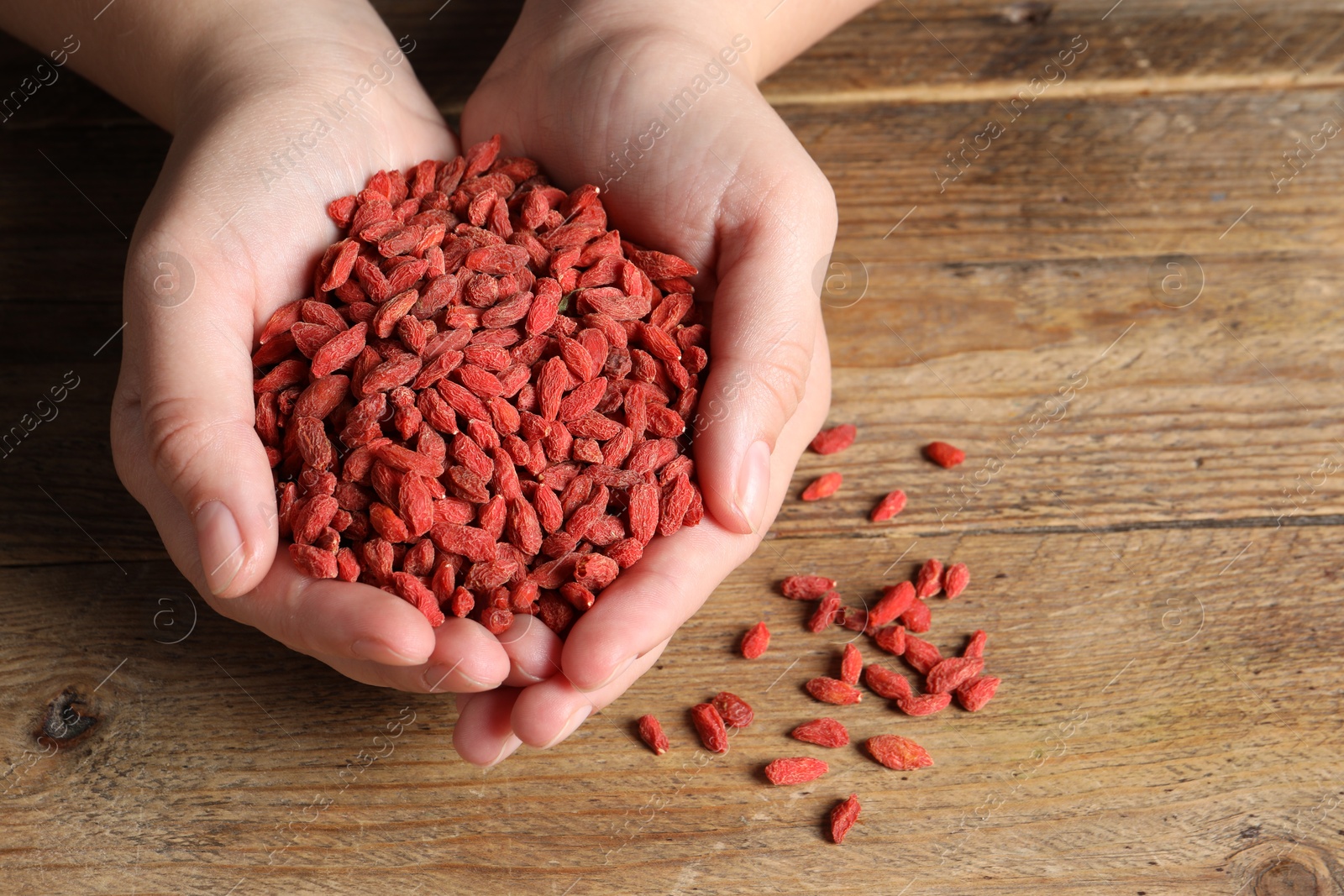Photo of Woman holding pile of dried goji berries at wooden table, top view