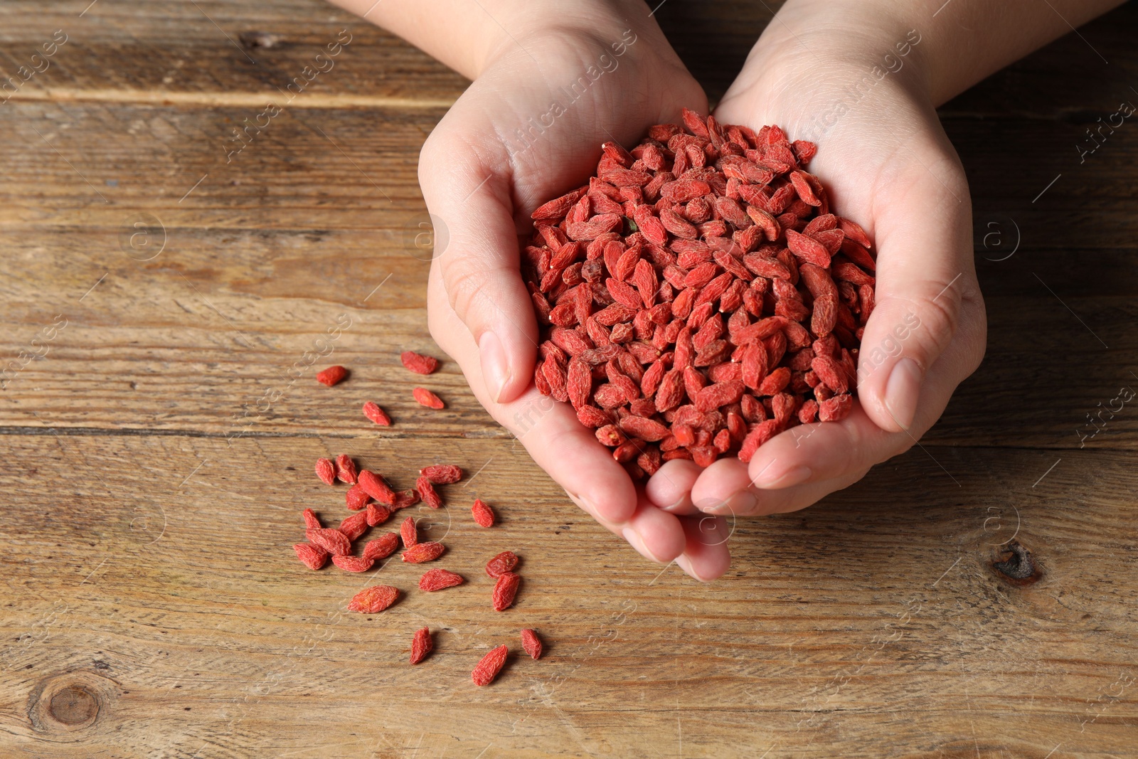 Photo of Woman holding pile of dried goji berries at wooden table, top view