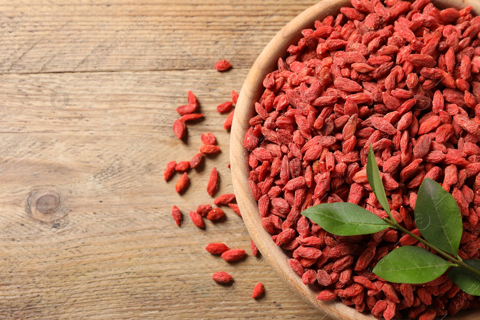 Photo of Dried goji berries and leaves in bowl on wooden table, top view. Space for text