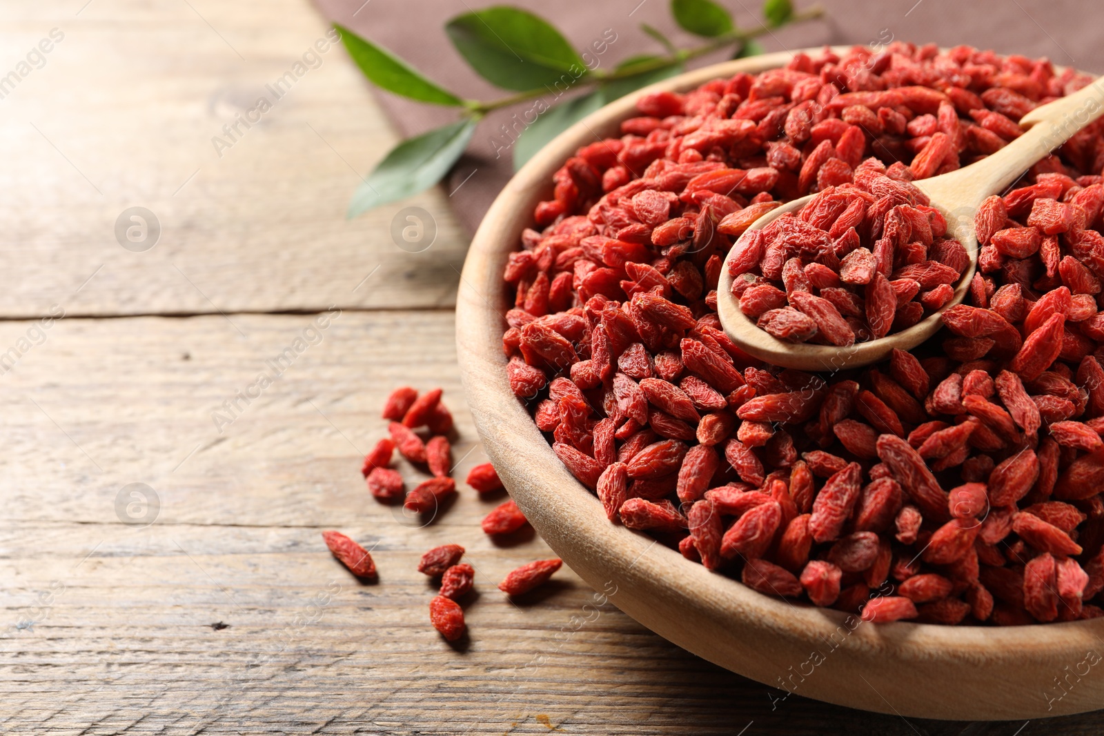 Photo of Dried goji berries in bowl and spoon on wooden table, closeup. Space for text