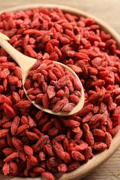 Photo of Dried goji berries in bowl and spoon on wooden table, closeup