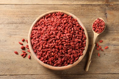 Photo of Dried goji berries in bowl and spoon on wooden table, flat lay