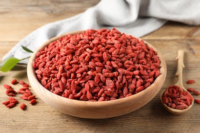 Dried goji berries in bowl and spoon on wooden table, closeup