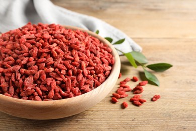 Photo of Dried goji berries in bowl on wooden table, closeup. Space for text