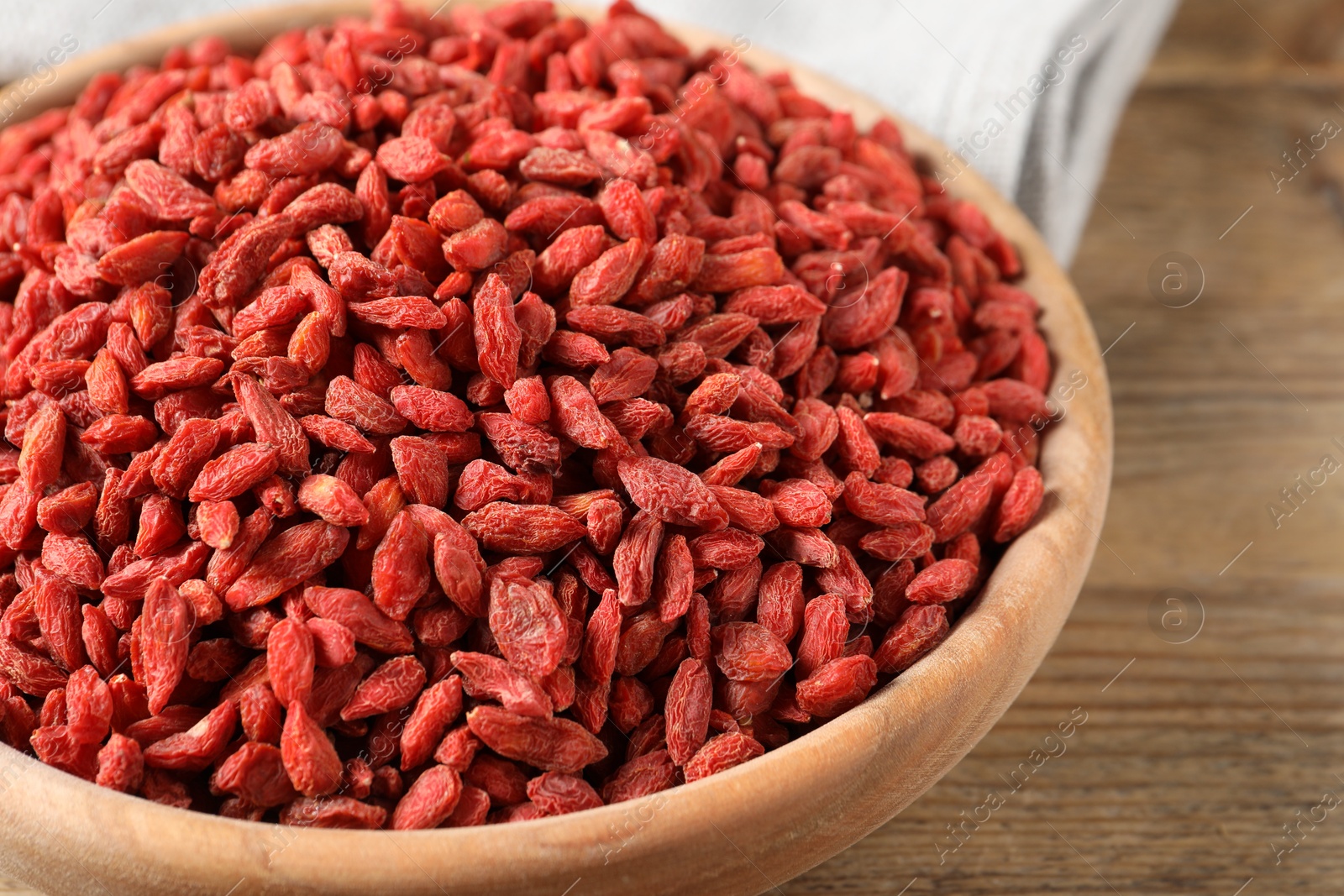 Photo of Dried goji berries in bowl on wooden table, closeup