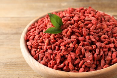 Photo of Dried goji berries in bowl on wooden table, closeup