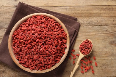 Photo of Dried goji berries in bowl and spoon on wooden table, flat lay