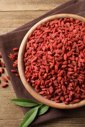 Photo of Dried goji berries in bowl and leaves on wooden table, flat lay