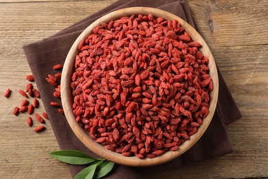 Photo of Dried goji berries in bowl and leaves on wooden table, flat lay