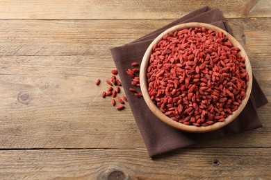 Photo of Dried goji berries in bowl on wooden table, top view. Space for text