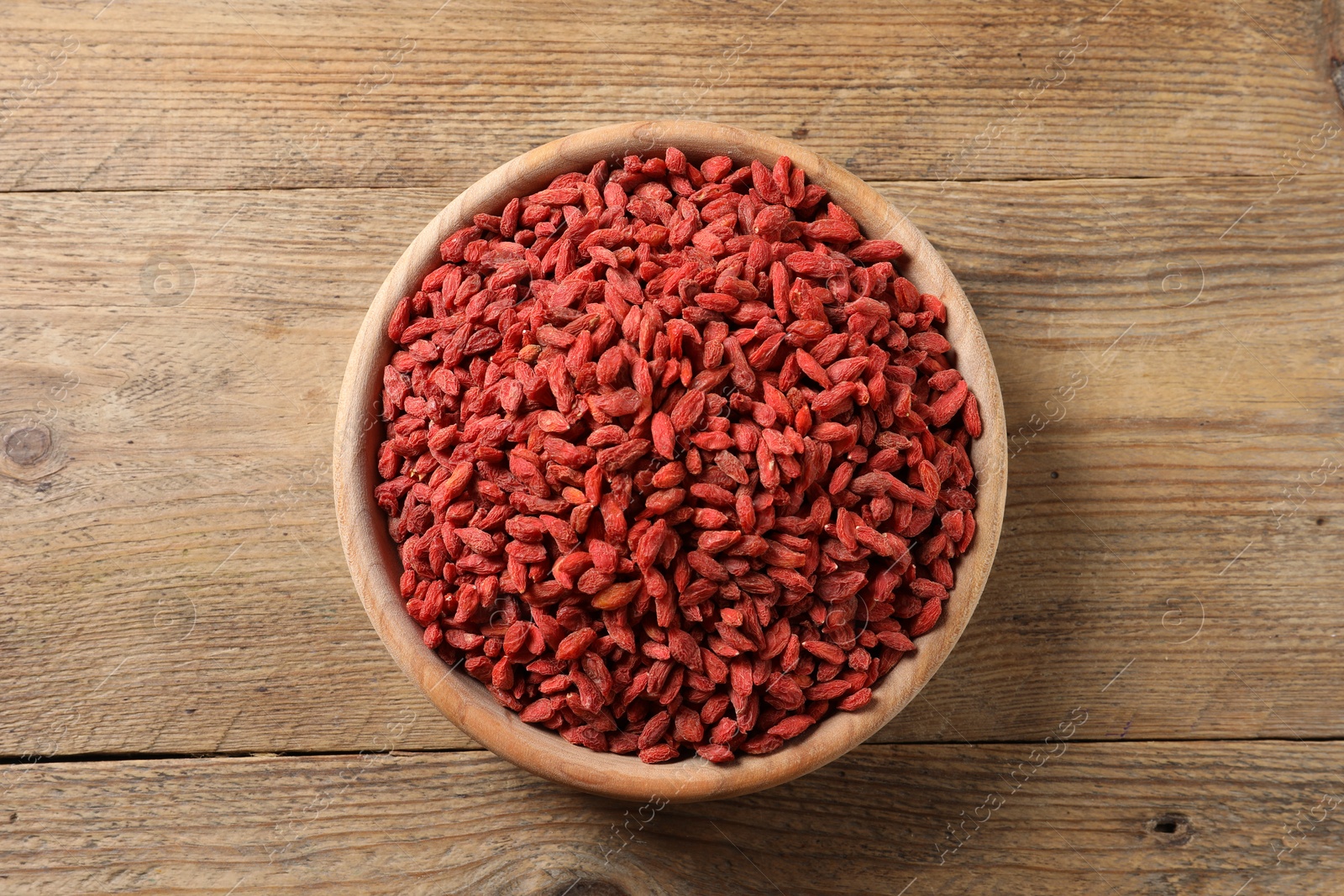 Photo of Dried goji berries in bowl on wooden table, top view