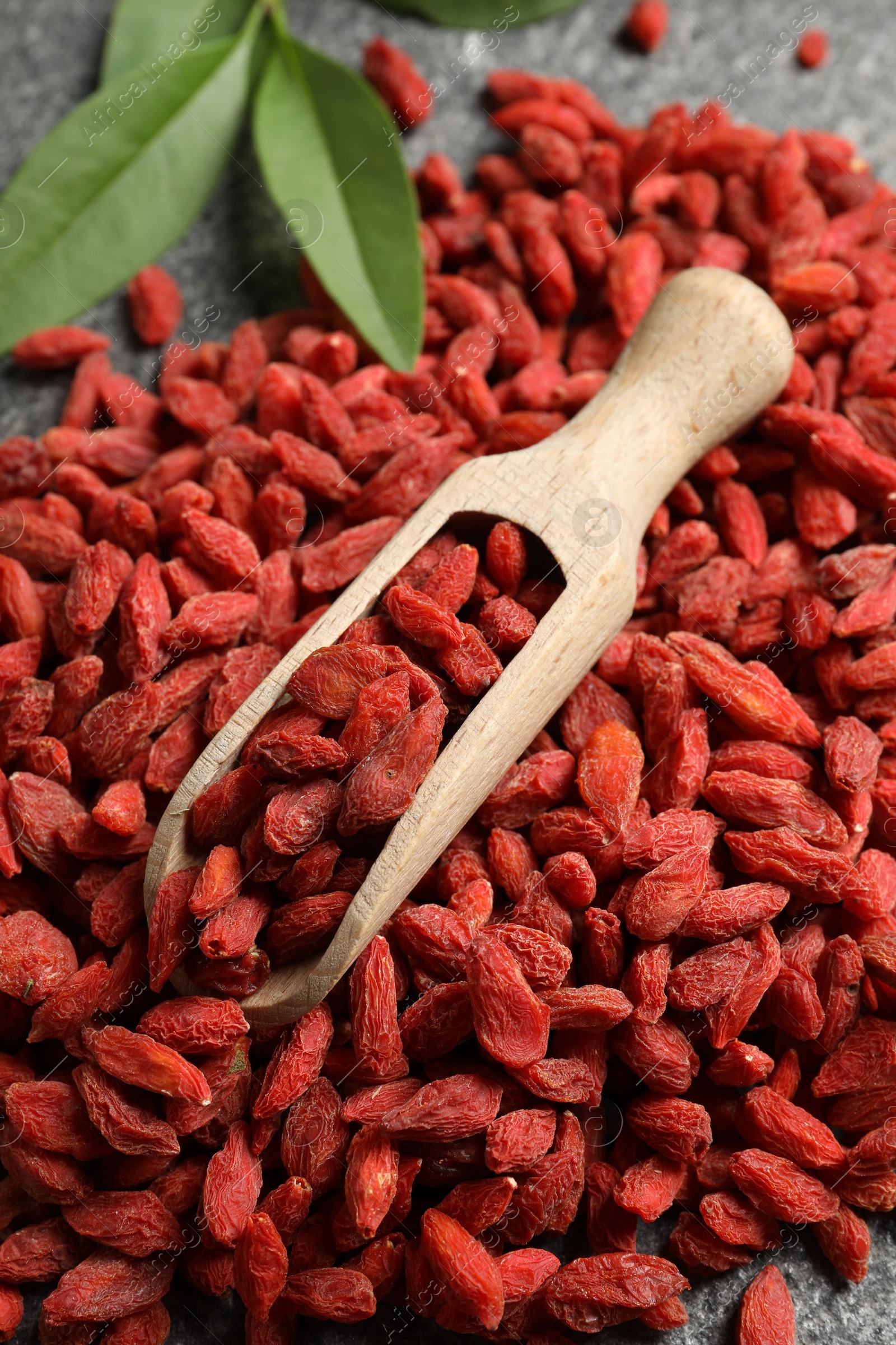 Photo of Dried goji berries and scoop on grey textured table, above view