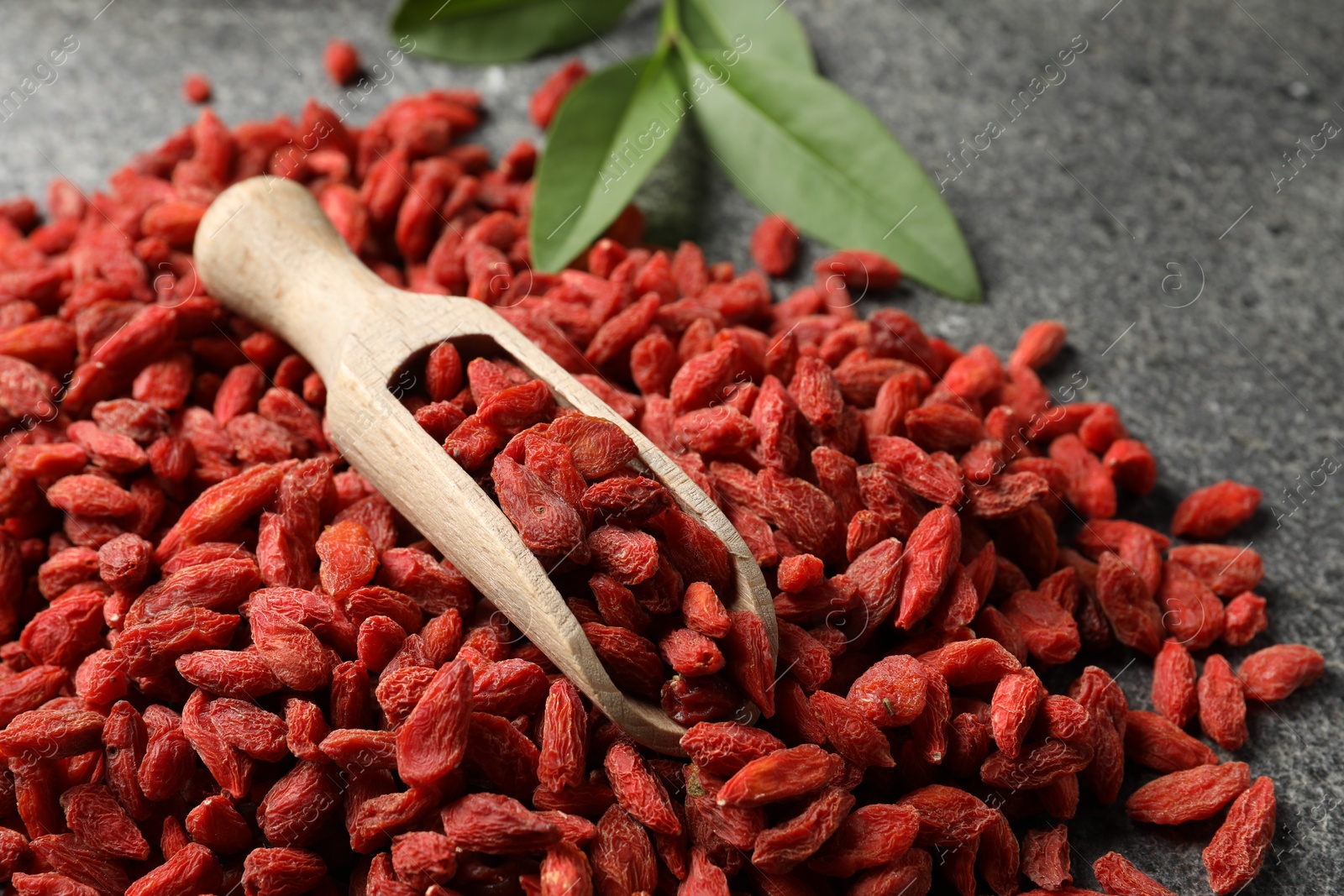 Photo of Dried goji berries and scoop on grey textured table, closeup