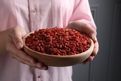 Woman holding bowl with dried goji berries near grey wall, closeup