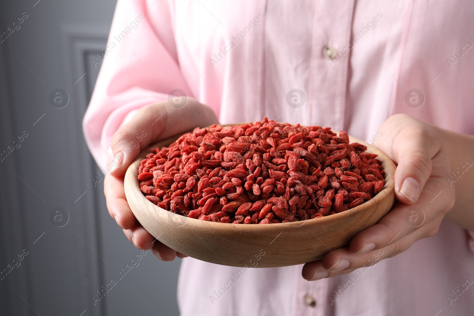 Photo of Woman holding bowl with dried goji berries near grey wall, closeup