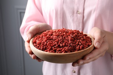 Woman holding bowl with dried goji berries near grey wall, closeup