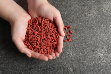 Photo of Woman holding pile of dried goji berries on grey textured table, top view. Space for text