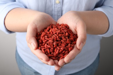 Photo of Woman holding pile of dried goji berries on grey background, closeup