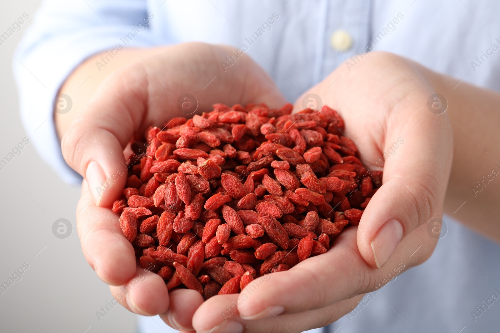 Photo of Woman holding pile of dried goji berries on grey background, closeup