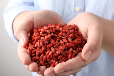 Photo of Woman holding pile of dried goji berries on grey background, closeup