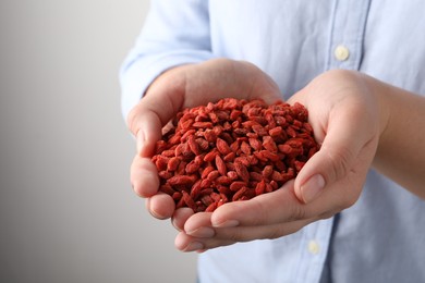 Woman holding pile of dried goji berries on grey background, closeup. Space for text