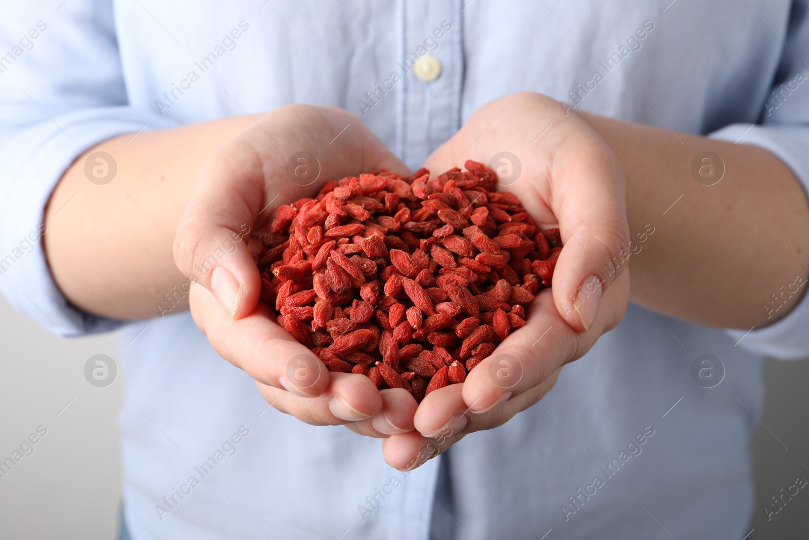 Photo of Woman holding pile of dried goji berries on grey background, closeup