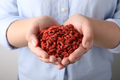 Woman holding pile of dried goji berries on grey background, closeup