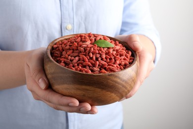 Photo of Woman holding bowl with dried goji berries on grey background, closeup