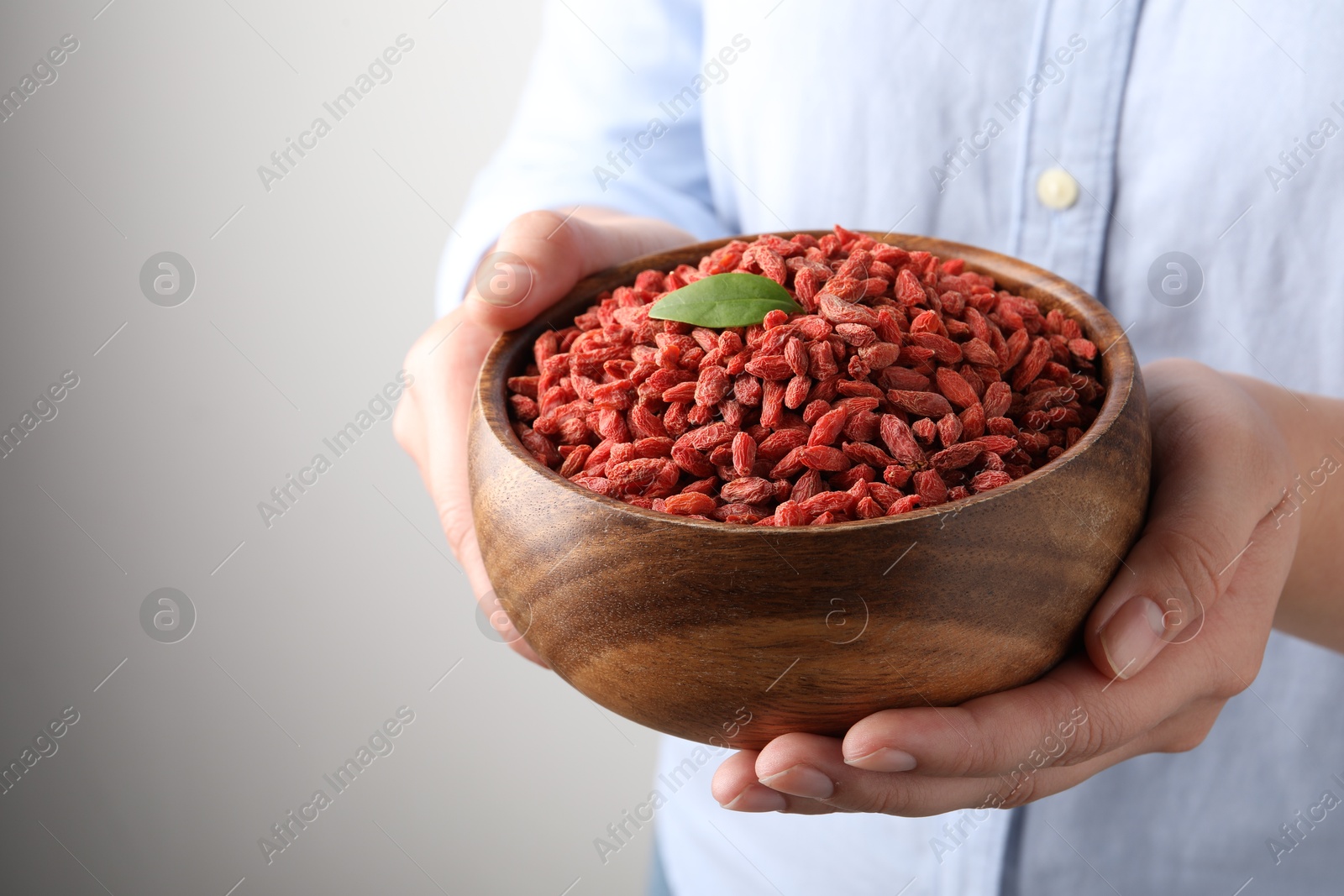 Photo of Woman holding bowl with dried goji berries on grey background, closeup. Space for text