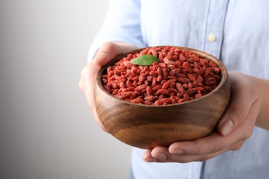 Photo of Woman holding bowl with dried goji berries on grey background, closeup. Space for text