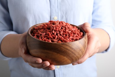 Woman holding bowl with dried goji berries on grey background, closeup