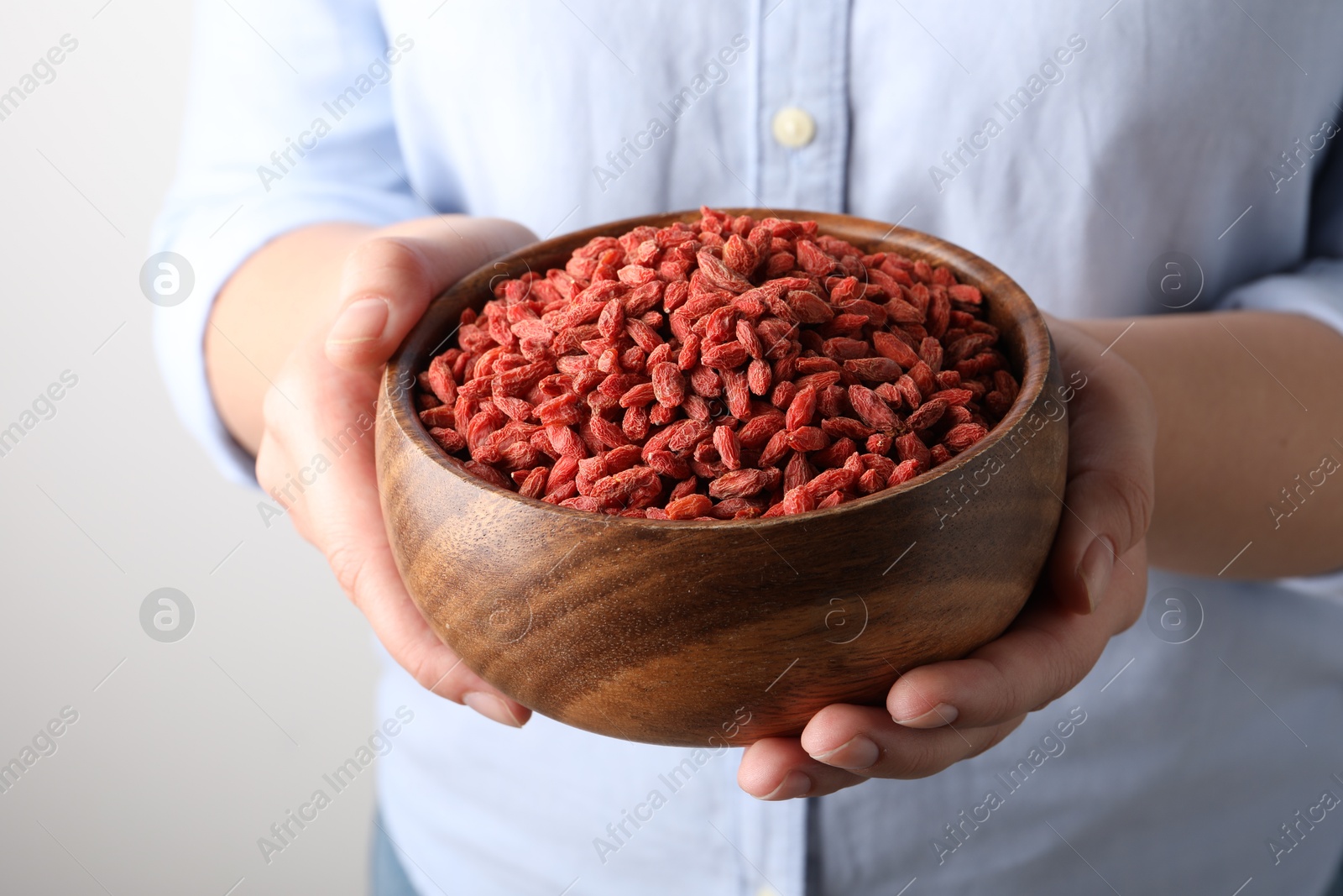 Photo of Woman holding bowl with dried goji berries on grey background, closeup