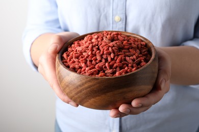 Photo of Woman holding bowl with dried goji berries on grey background, closeup