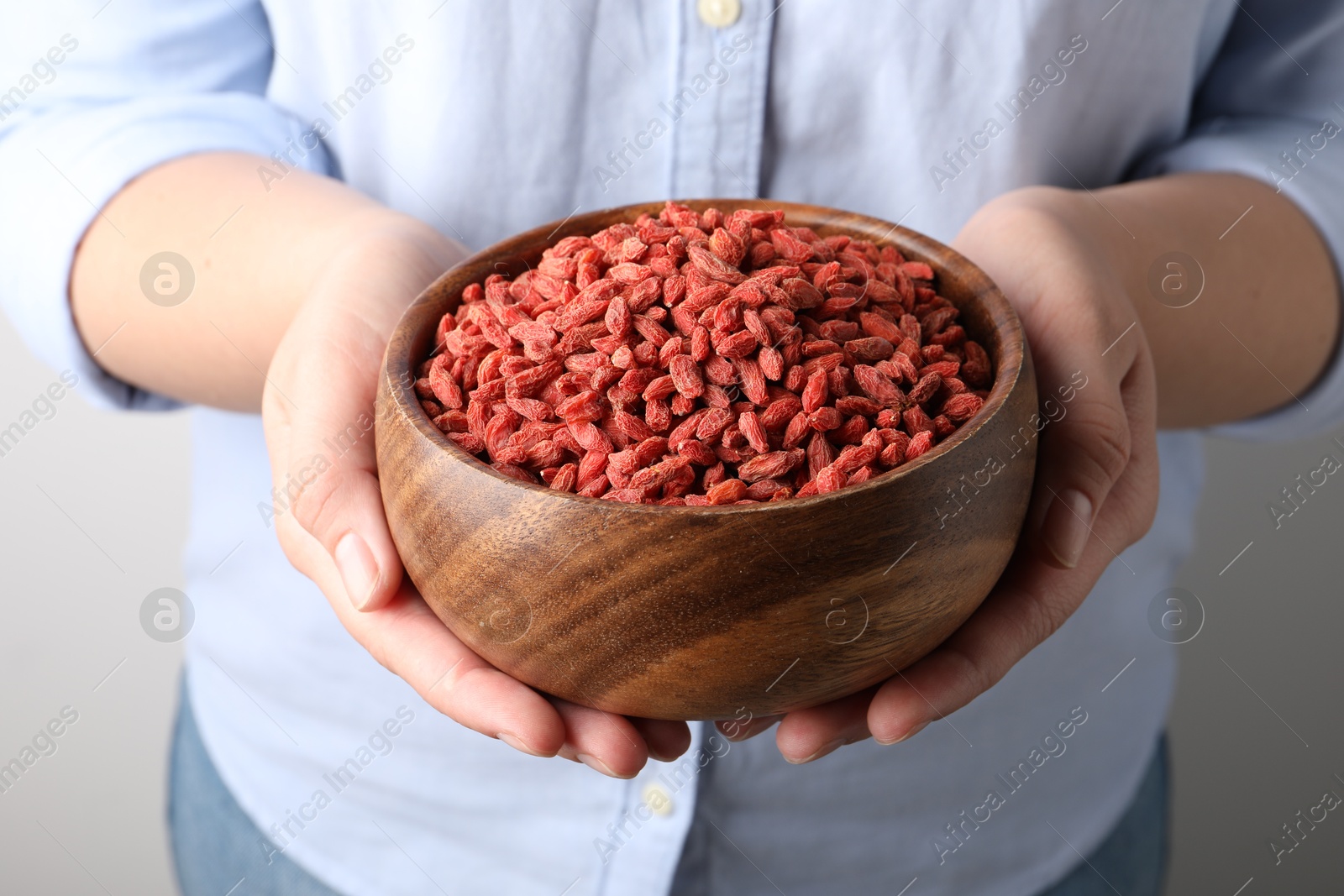 Photo of Woman holding bowl with dried goji berries on grey background, closeup