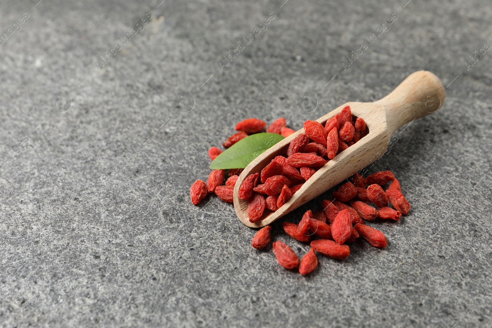 Photo of Dried goji berries and wooden scoop on grey textured table. Space for text