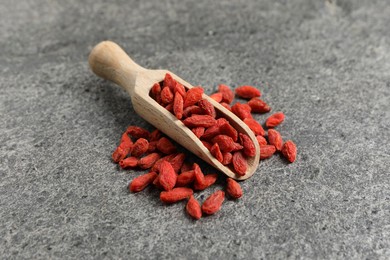 Photo of Dried goji berries and wooden scoop on grey textured table, closeup