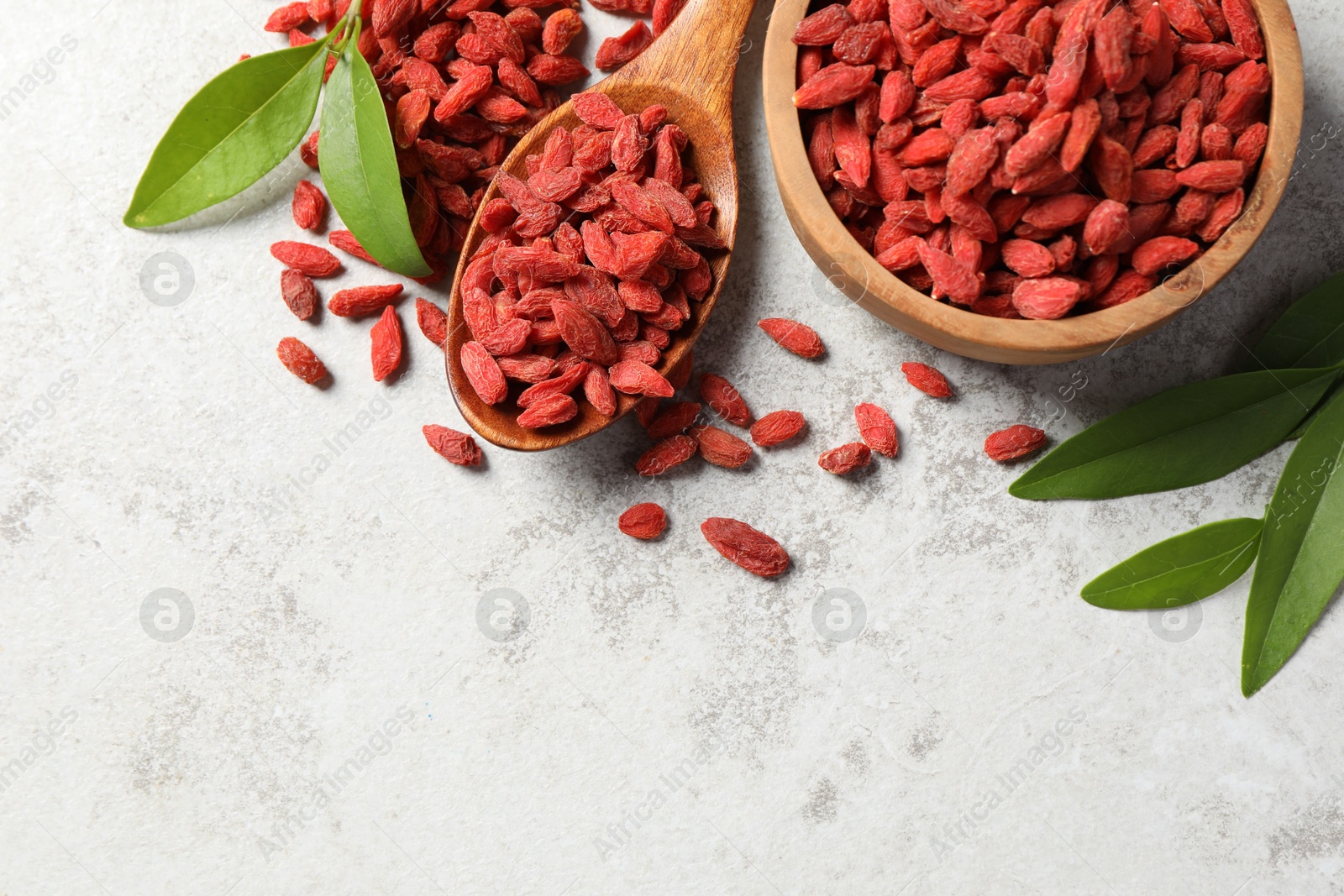 Photo of Dried goji berries and leaves on grey textured table, flat lay. Space for text