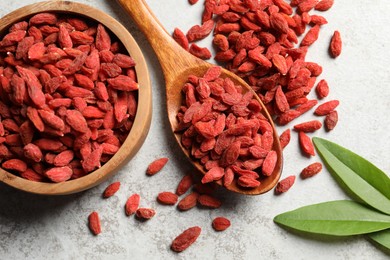 Dried goji berries and leaves on grey textured table, flat lay