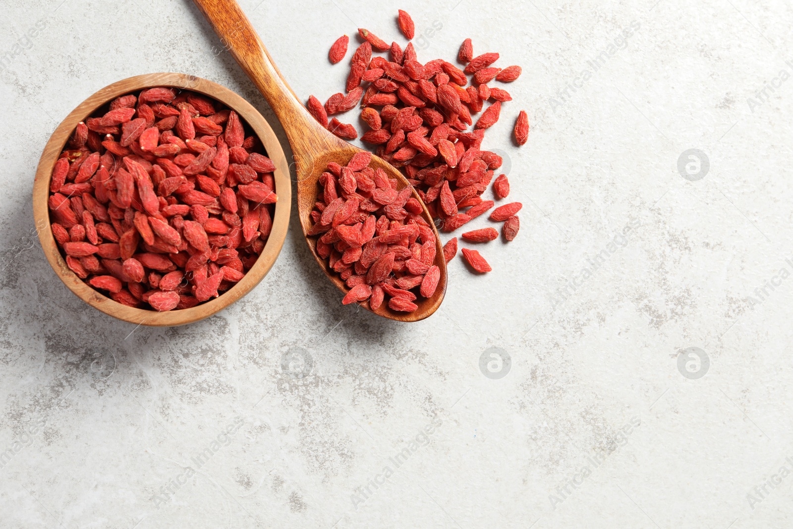 Photo of Dried goji berries, bowl and spoon on grey textured table, flat lay. Space for text