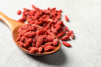 Photo of Spoon with dried goji berries on grey textured table, closeup