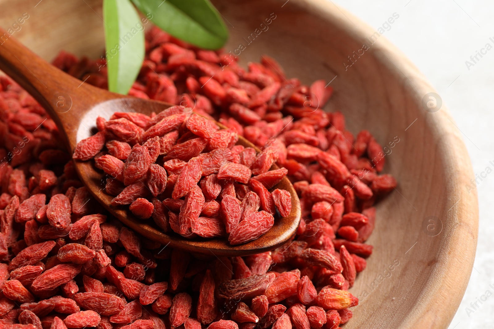 Photo of Dried goji berries and spoon in wooden bowl on light background, closeup