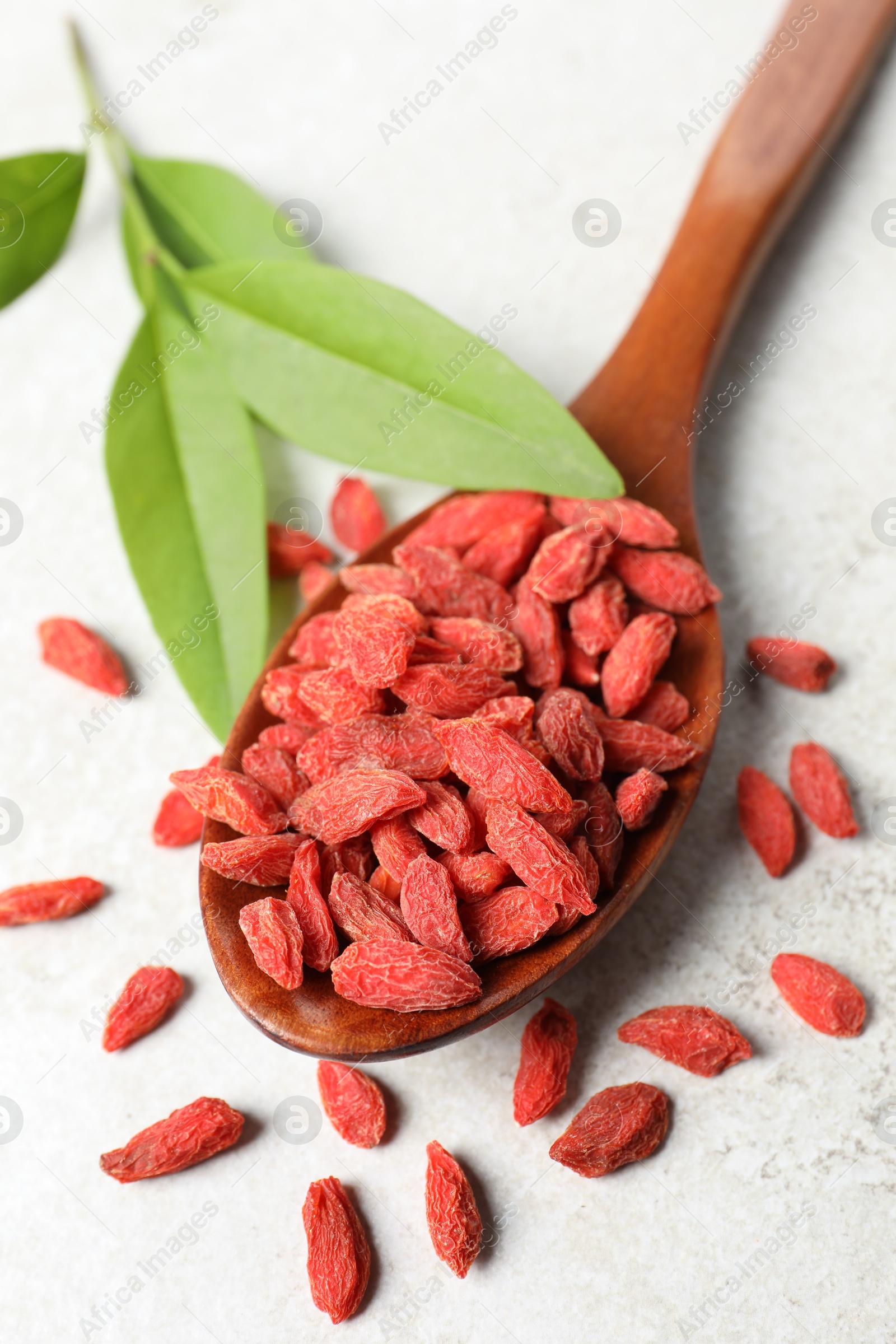 Photo of Dried goji berries, leaves and spoon on light textured table, above view