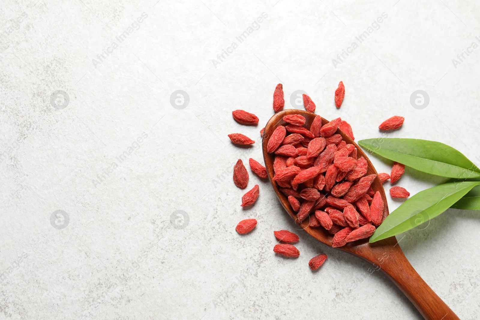 Photo of Dried goji berries, leaves and spoon on light textured table, flat lay. Space for text