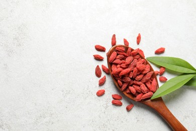 Photo of Dried goji berries, leaves and spoon on light textured table, flat lay. Space for text