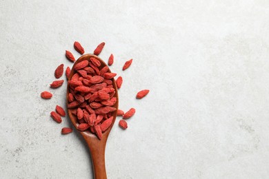 Photo of Dried goji berries and spoon on light textured table, flat lay. Space for text